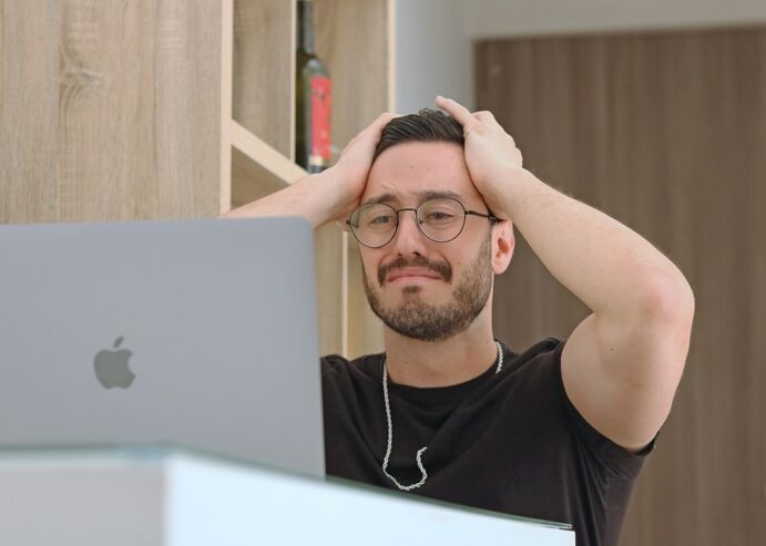 a man with glasses is frowning while looking at a laptop 
